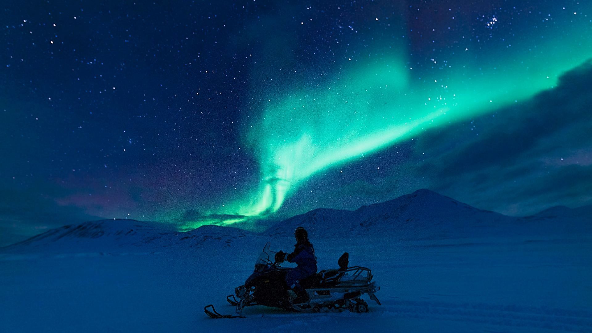 Snescooter p&aring; tur i den bl&aring; time med gr&oslash;nt norslys p&aring; himlen